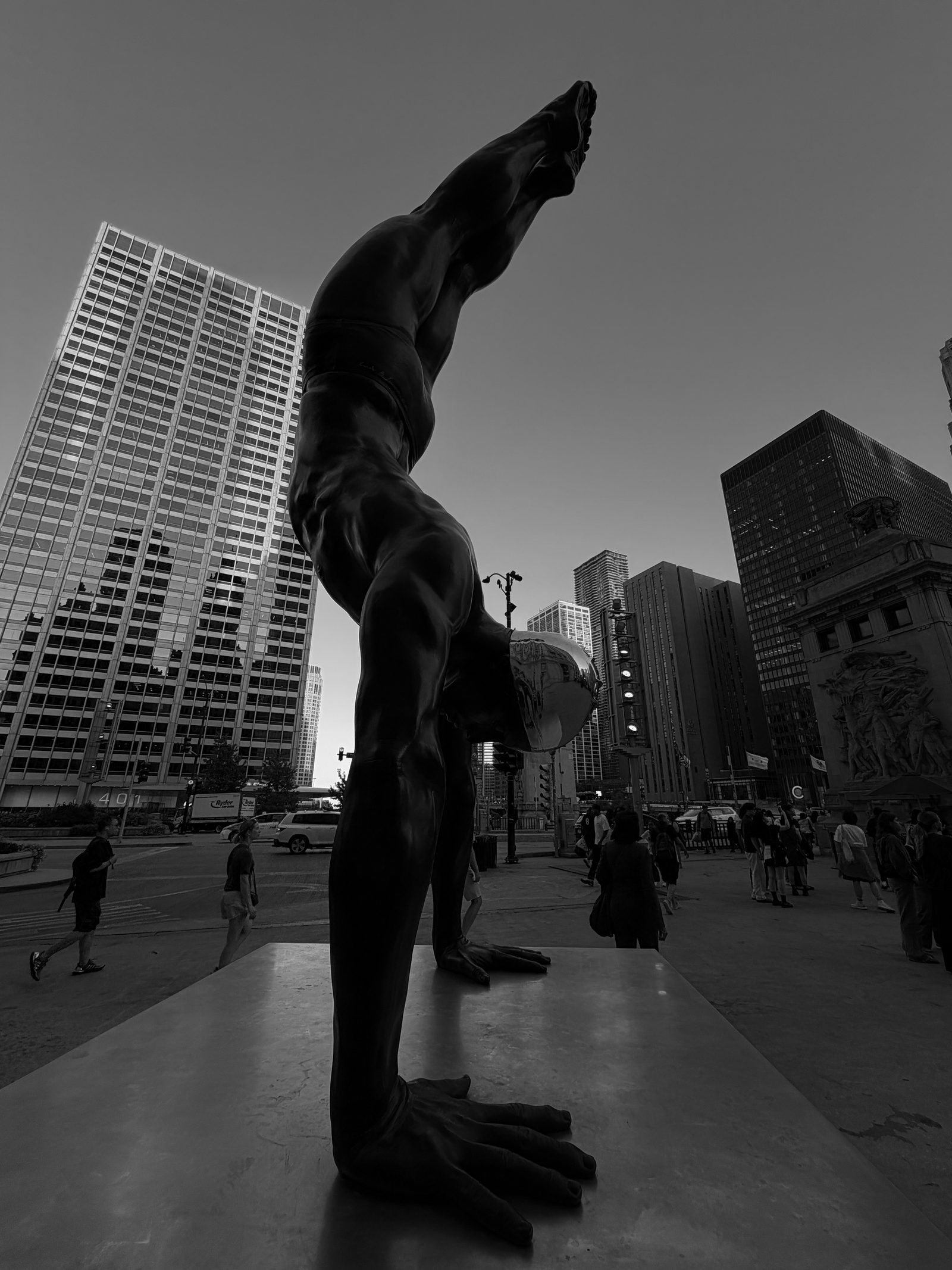 A bronze figure in a handstand beside a mirrored sphere, viewed from below against Chicago buildings.