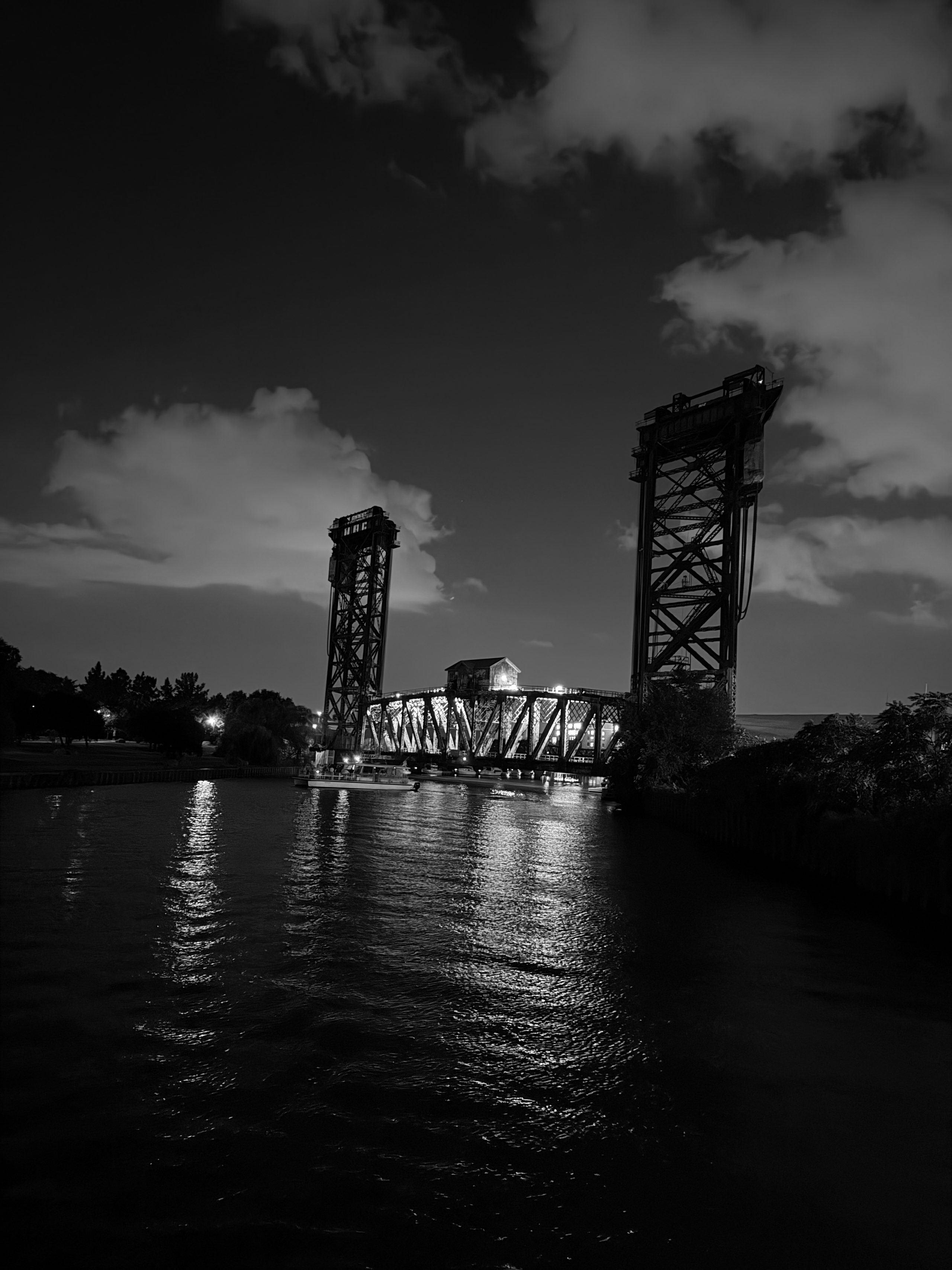 A raised steel bascule bridge and its towers reflected in the Chicago River at dusk.