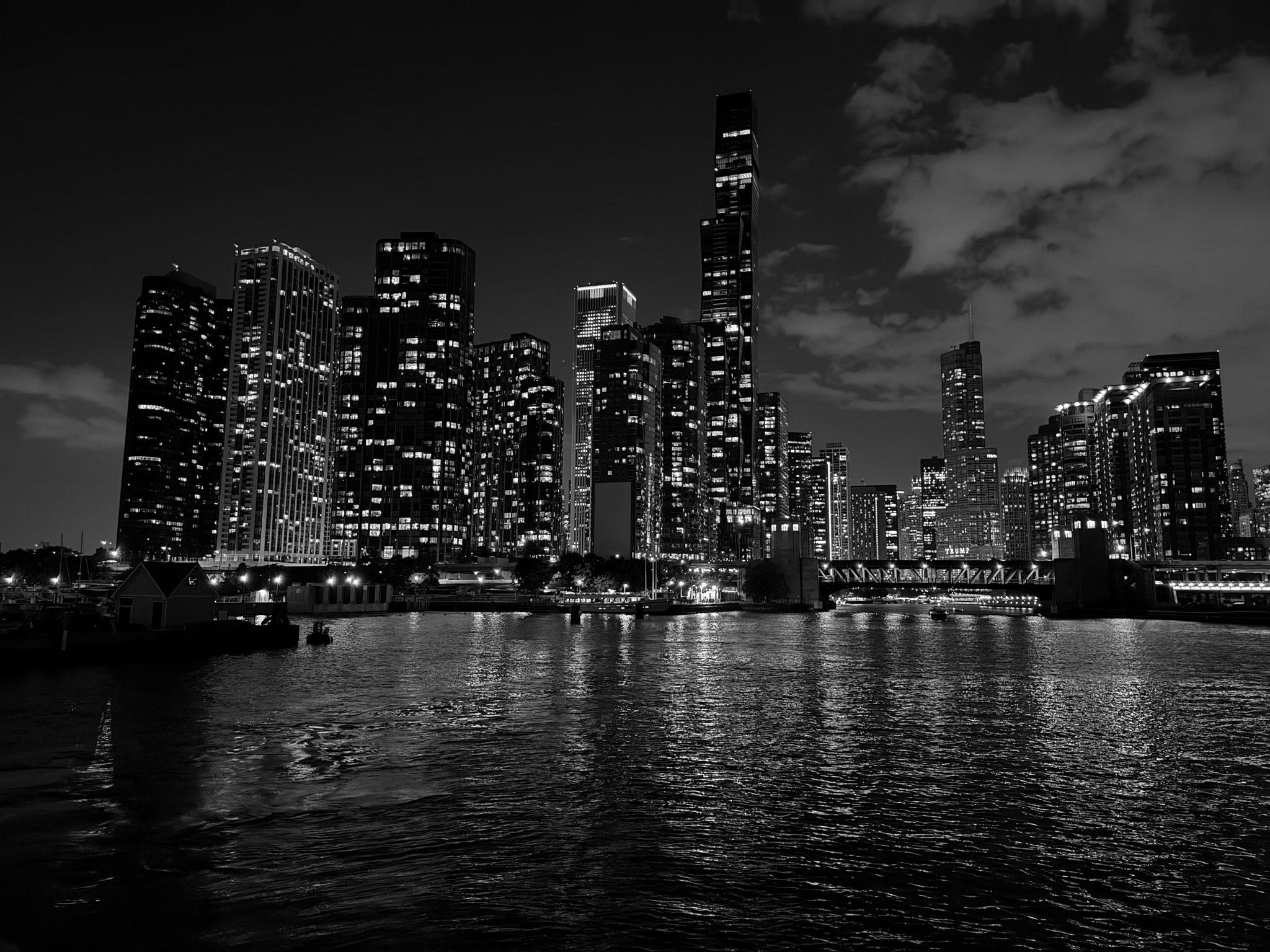 Illuminated high-rises reflected in the Chicago River, with a boathouse along the near bank.