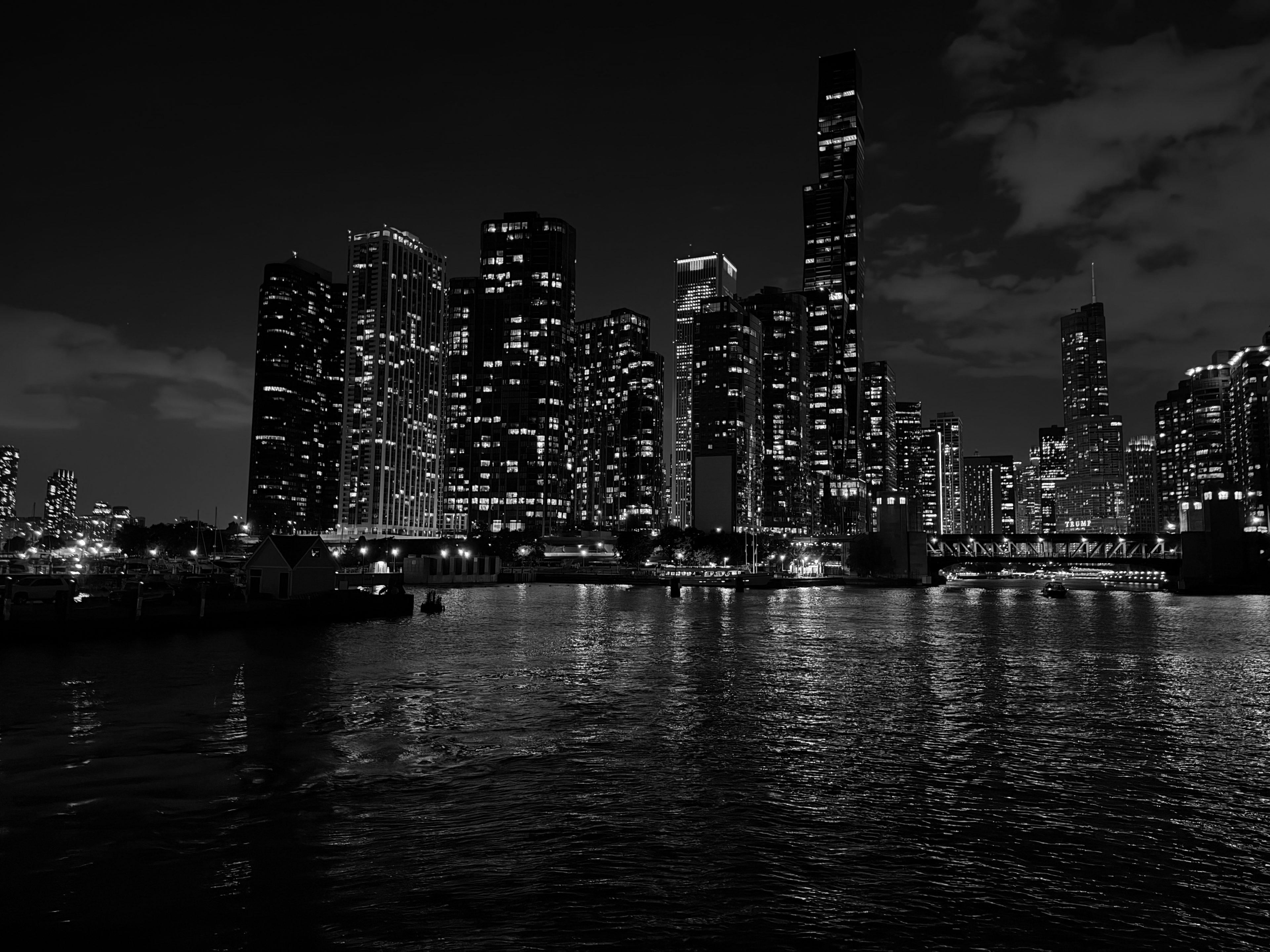 The illuminated Chicago skyline mirrored in calm river water, with boats beside a lit dock.