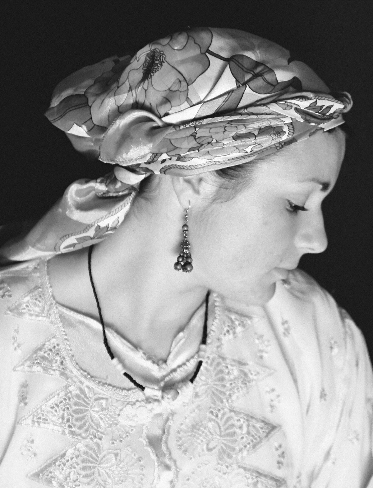 A woman wearing a patterned headscarf looks down in a softly lit portrait.