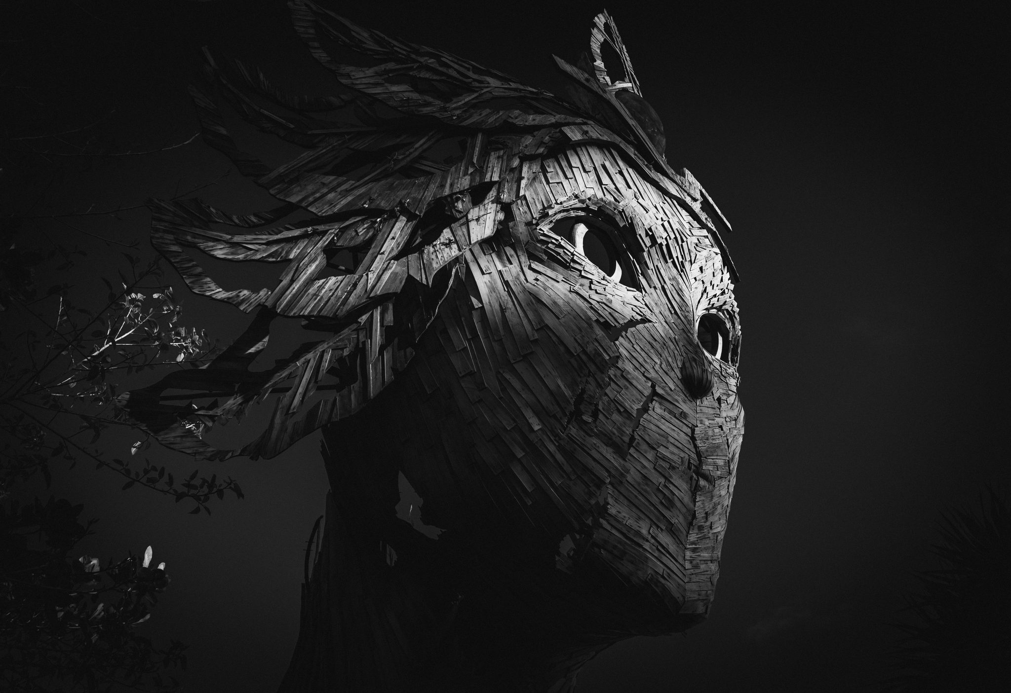 A close view of a sculpted face made from textured natural fibres, with flowing strands extending into darkness.