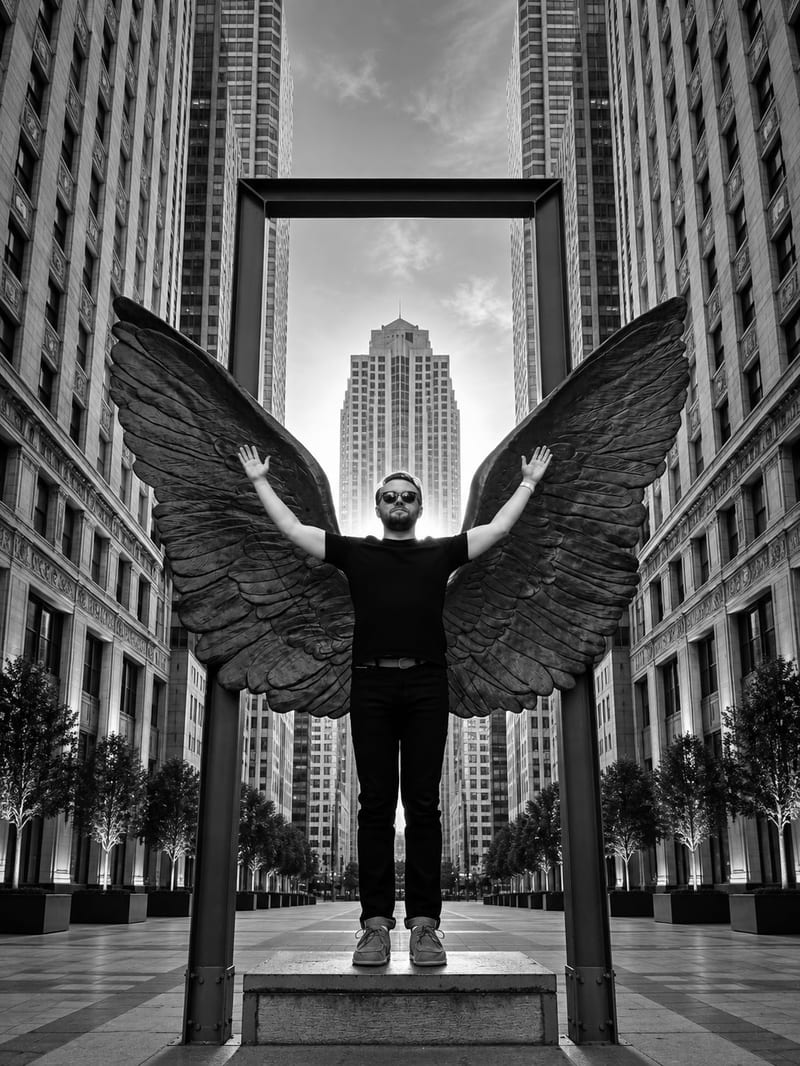 Tomasz Nowicki standing with his arms raised in front of a wing sculpture between Chicago skyscrapers.